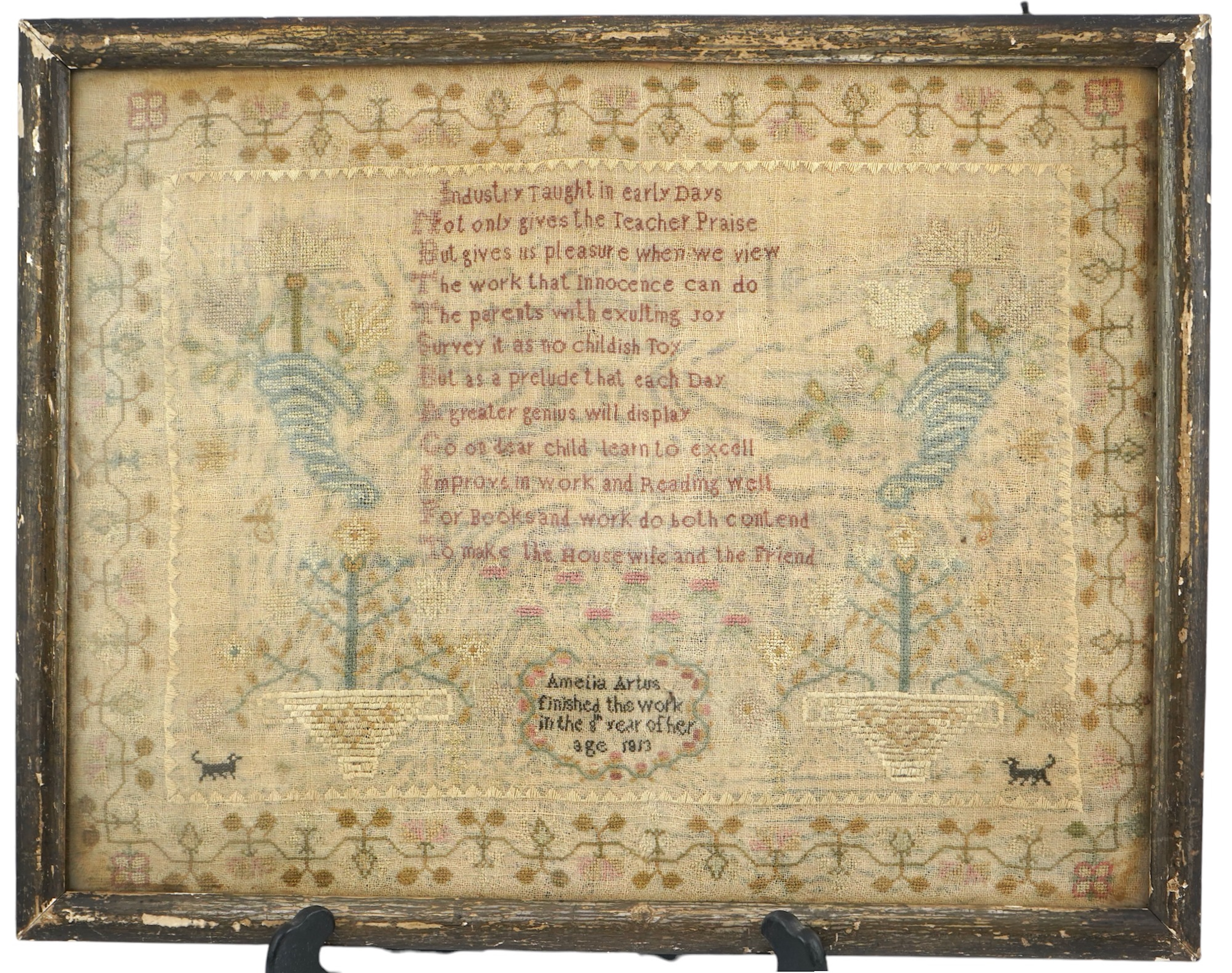 A gilt framed finely worked Regency gauze sampler, by Amelia Artus, aged 8 years, dated 1813, worked on fine gauze with coloured silk threads, with a large central panel having a long verse, two motifs of cornucopia, pot